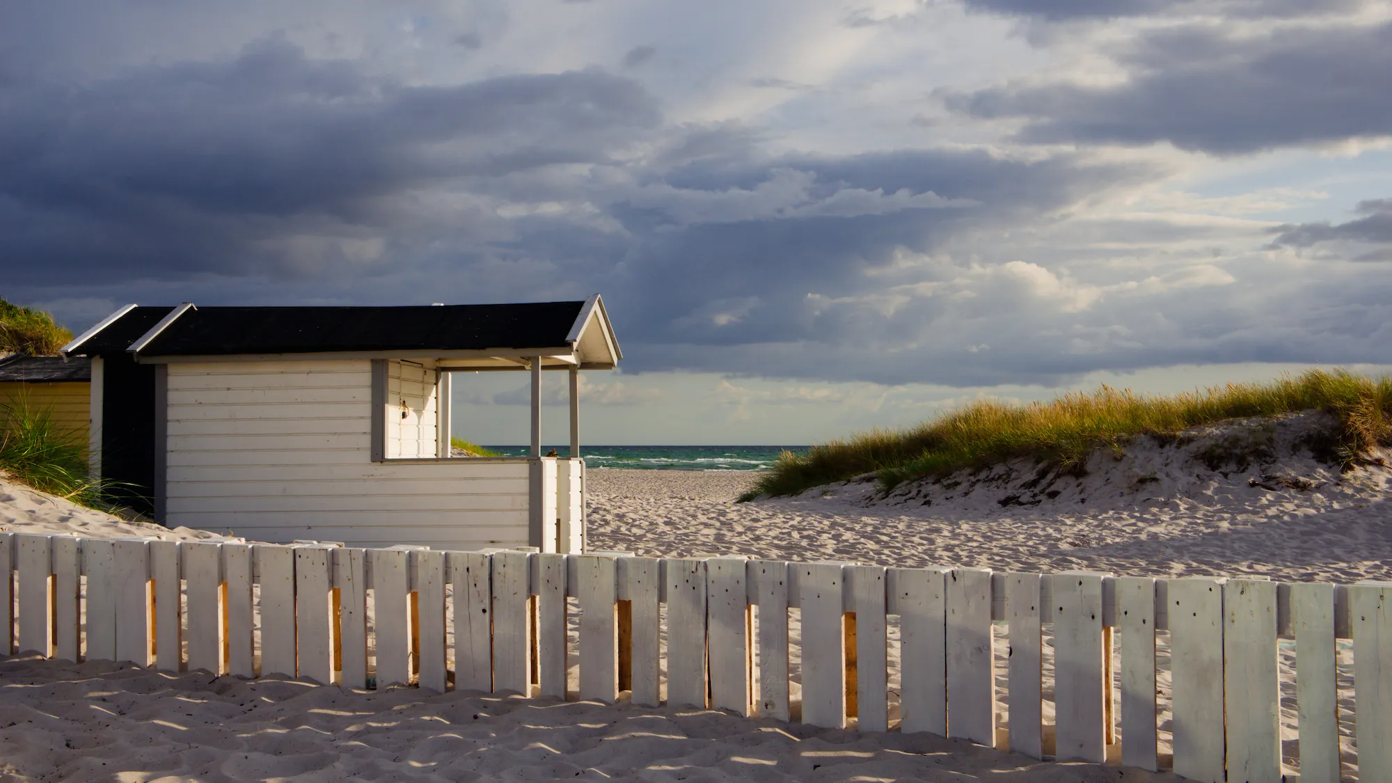 After: beach cabin under storm clouds, with the preset inspired by Fujifilm Velvia 50 (GA — 014 / P): deep, saturated blues.